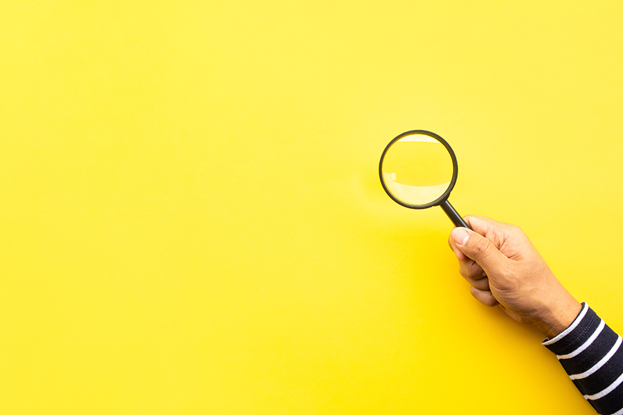 Hand holding magnifying glass against yellow background.