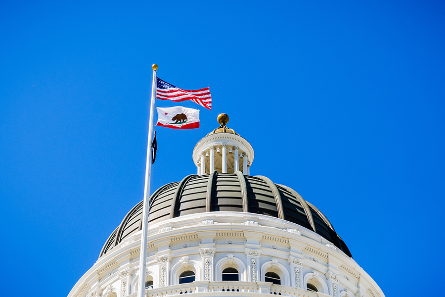 Top of the California State capital dome with state and US flags on flagpole.