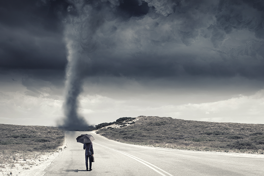 Man with umbrella walking on road toward tornado that has touch ground.