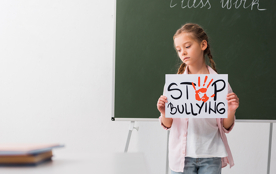 Girl in classroom holding up Stop Bullying sign.