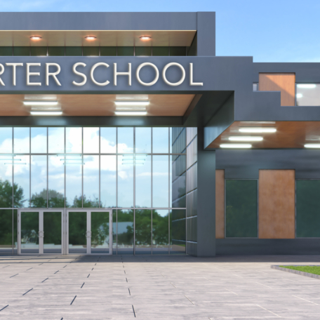 A modern charter school building boasts a large glass entrance, flat roof, and angular design. The sign proudly displays "Charter School." Trees line the paved walkway in the foreground, offering an inviting path to education excellence.