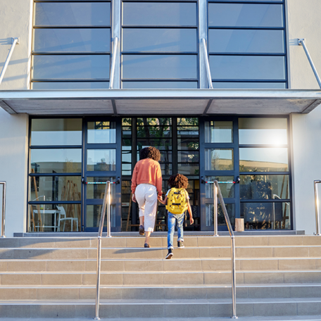 Mom and child holding hands on steps of campus entrance for back to school.