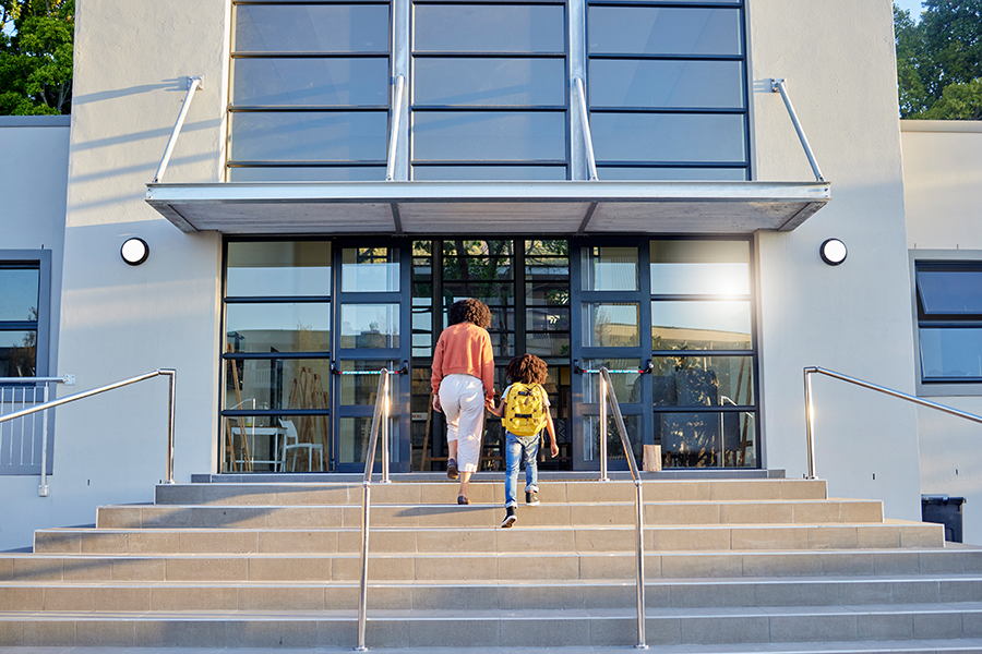 Mom and child holding hands on steps of campus entrance for back to school.