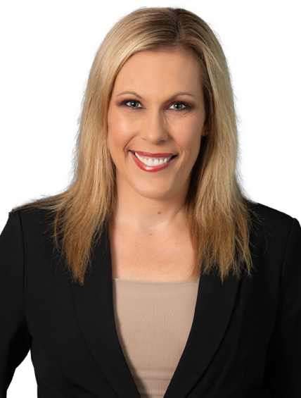 Blonde woman in a black blazer over a beige top, smiling against a dark blue patterned background.