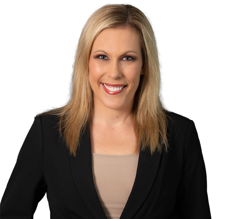 Blonde woman in a black blazer over a beige top, smiling against a dark blue patterned background.