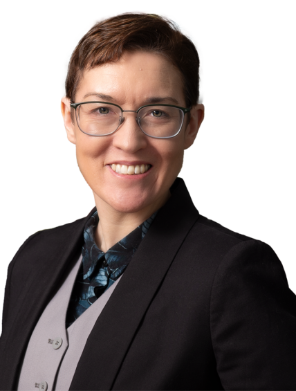 A person with short hair and glasses wearing a suit jacket and vest smiles at the camera, standing in front of a colorful, abstract background.