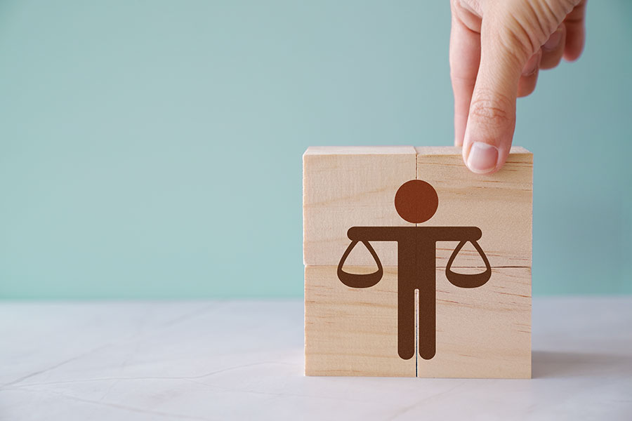 A hand arranges wooden blocks featuring a scale of justice icon against a green background, symbolizing the balanced approach of an education law firm.