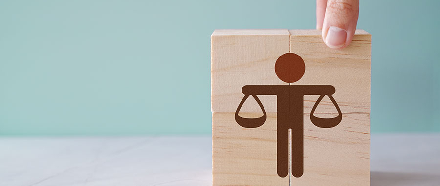 A hand arranges wooden blocks, one showcasing an icon of a person holding scales, symbolizing justice or balance—much like the careful equilibrium maintained in independent study.