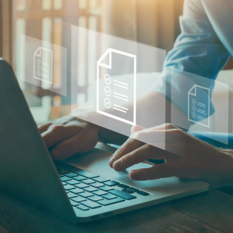 A person types on a laptop with floating digital document icons, illustrating online or cloud data management, while integrating ethics training seamlessly into the workflow.