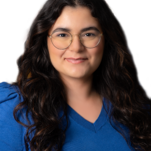 Annabella Yousif, Esq., is a woman with long wavy dark hair and glasses, wearing a blue sweater, poses in front of a white background.