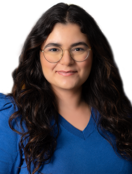 Annabella Yousif, Esq., is a woman with long wavy dark hair and glasses, wearing a blue sweater, poses in front of a white background.