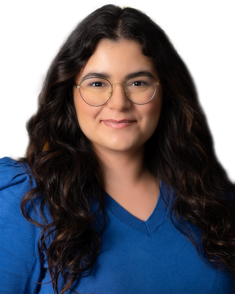 Annabella Yousif, Esq., is a woman with long wavy dark hair and glasses, wearing a blue sweater, poses in front of a white background.