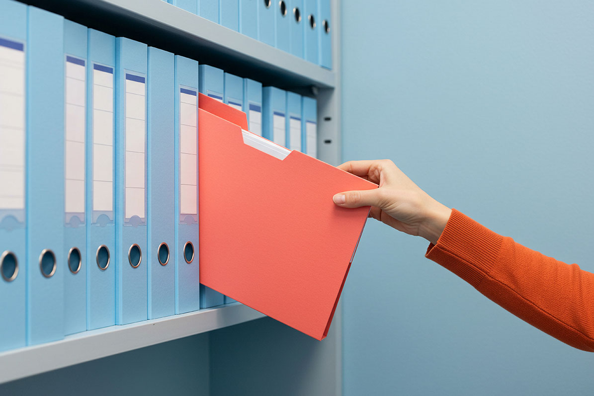 A person selects a red file folder—potentially containing FERPA-protected documents—from a shelf filled with blue binders in an office setting.