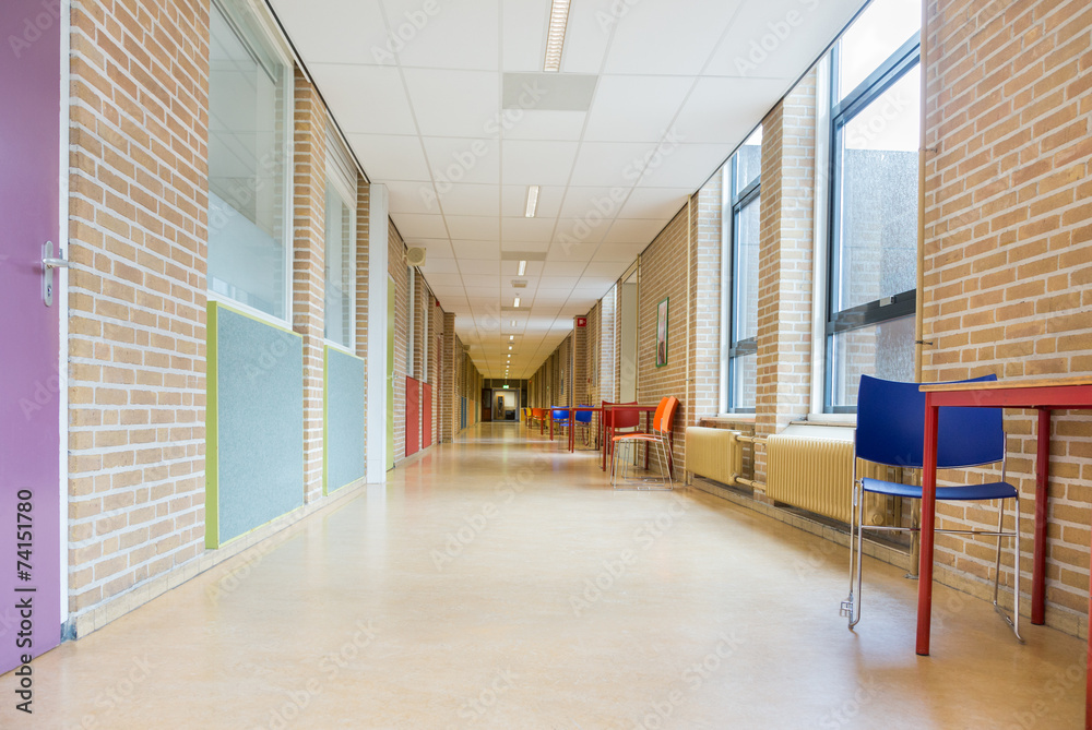 A wide hallway in a school or office building—with brick walls, large windows, tables, and colorful chairs—buzzes with excitement during charter renewal discussions.