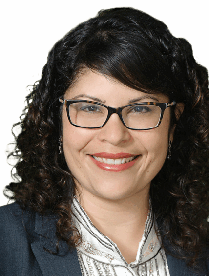 Sarah Bancroft, a woman with curly dark hair, glasses, and a dark blazer, smiles at the camera against a plain white background.